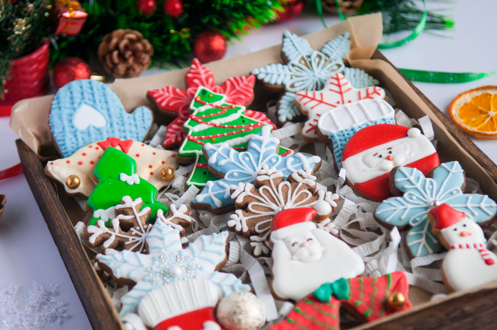 Assorted Christmas-themed cookies in a box with festive decorations in the background.