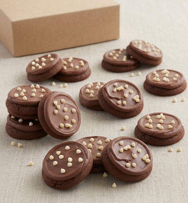 Twelve soft-baked double chocolate fudge buttercream frosted cookies topped with white chocolate chips, stacked and arranged on a white surface